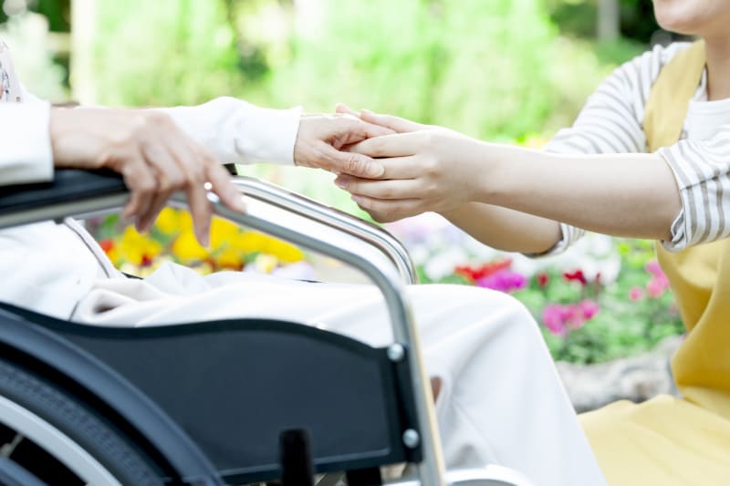 車いすに座る高齢女性の手を握る介護士の女性